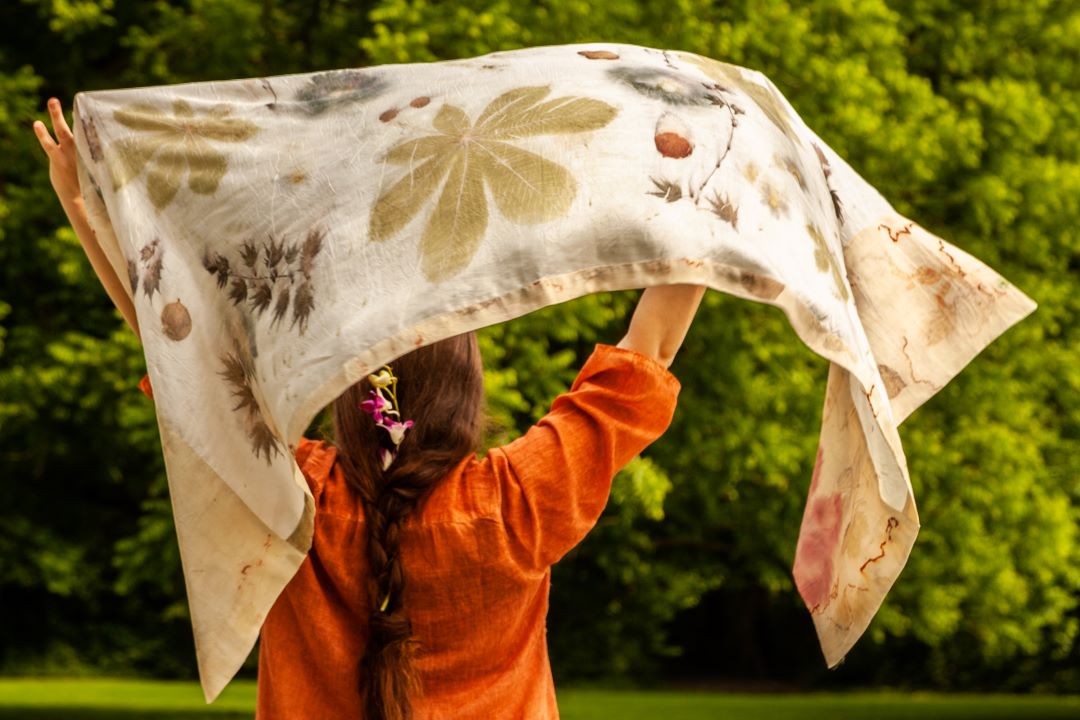 Una donna di spalle stende al vento una stola con stampe naturali